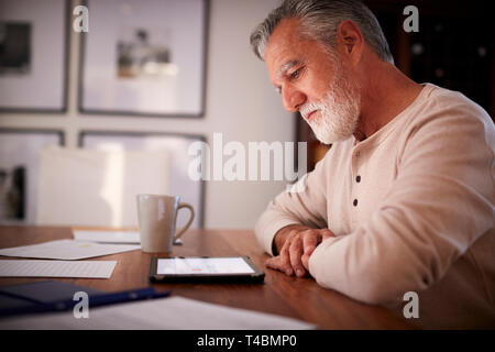 Senior Hispanic Mann an einem Tisch sitzen mit einem Tablet Computer am Abend, Nahaufnahme, Seitenansicht Stockfoto