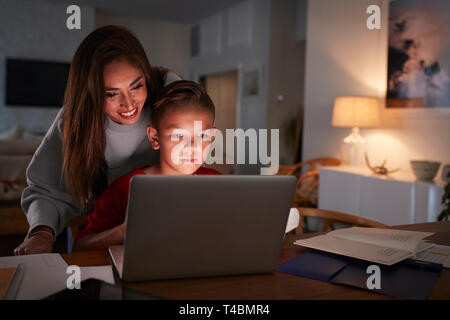 Hispanic Frau schaut über die Schulter ihres Sohnes, während er seine Hausaufgaben mit Laptop Stockfoto