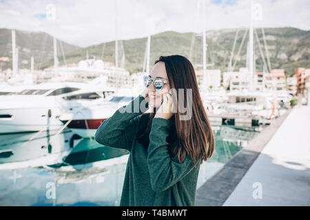 Schöne Mädchen, die sich in ein Handy auf dem Hintergrund der Yachten im Hafen von Porto Montenegro Kotor in Montenegro. Stockfoto