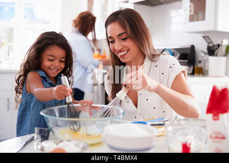 Junge Mädchen Kuchen in der Küche mit ihrer Mutter, Großmutter beschäftigt im Hintergrund, selektiver Fokus Stockfoto