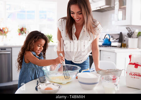 Junge hispanische Mädchen, Kuchen in der Küche, die von ihrer Mutter begleitet, Taille bis Stockfoto