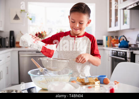 Pre-teen Boy hinzufügen Mehl zu Backmischung in der Küche auf seinen eigenen, Lächeln, Nahaufnahme Stockfoto