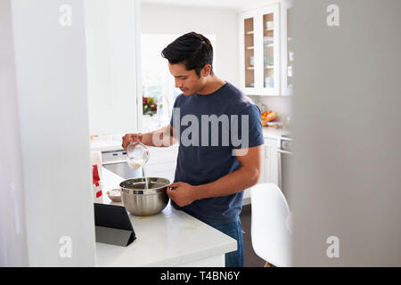 Tausendjährige Hispanic Mann Vorbereitung Kuchenteig in Küche, ein Rezept auf einem Tablet-PC Stockfoto