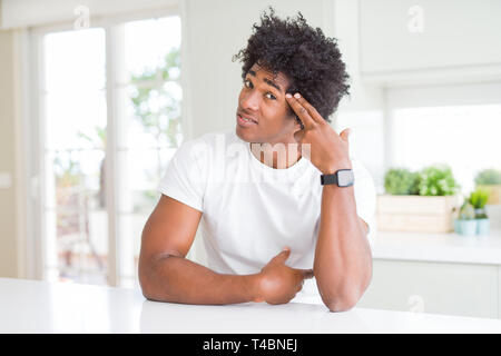 Junge afrikanische amerikanische Mann legere weißes T-shirt zu Hause sitzen Schießen und Töten sich zeigende Hand und Finger zu Kopf wie Pistole, suici Stockfoto