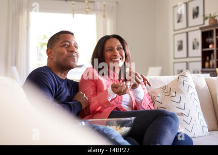 In der Nähe von Paar mittleren Alters saß auf dem Sofa im Wohnzimmer fernsehen, lachen und essen Popcorn, Nahaufnahme Stockfoto