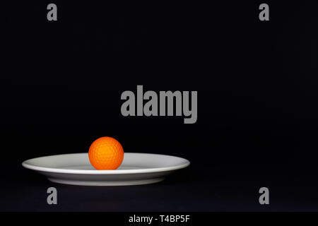 Weiße Platte und orange Golf Ball auf dem schwarzen Hintergrund Stockfoto