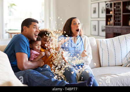 Jungen gemischten Rennen Familie sitzen zusammen auf dem Sofa im Wohnzimmer fernsehen scary movie versehentlich werfen Popcorn in der Luft Stockfoto