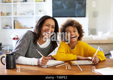 Mittleren Alters gemischten Rasse Frau am Tisch sitzen in Ihrem Esszimmer Zeichnung mit ihr vor - jugendlich Enkelin, in die Kamera lachen, Vorderansicht, in der Nähe