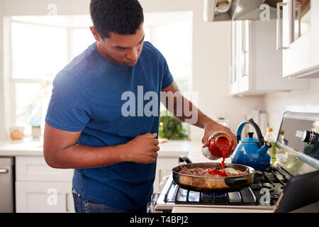 Junge Erwachsene schwarze Mann in der Küche Kochen auf dem Herd, Hinzufügen einer Sauce in die Pfanne, in der Nähe Stockfoto
