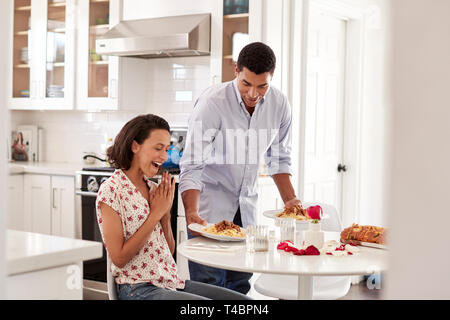 Jungen gemischten Rennen erwachsene Frau am Tisch sitzen in der Küche, ihr Partner ihr überraschend durch ein romantisches Essen, selektiver Fokus Stockfoto