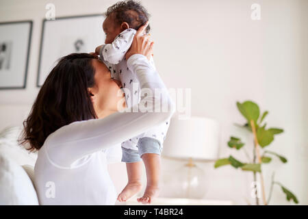 Happy gemischten Rennen junge Erwachsene Mutter ihre drei Monate alten Baby Sohn in die Luft und küsste seinen Bauch, Nahaufnahme, Seitenansicht Stockfoto
