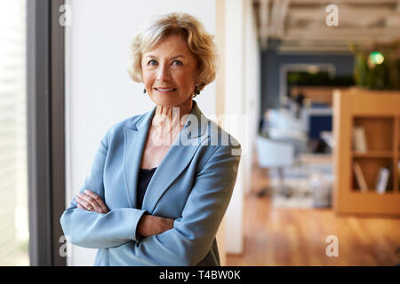 Portrait von lächelnden Senior Geschäftsfrau in modernen Büro stehen, Fenster Stockfoto