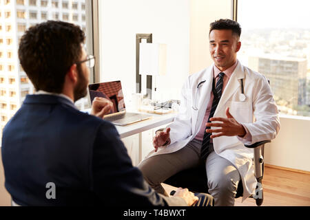 Blick über die Schulter des Mannes in Absprache mit männlicher Arzt im Krankenhaus Büro Stockfoto