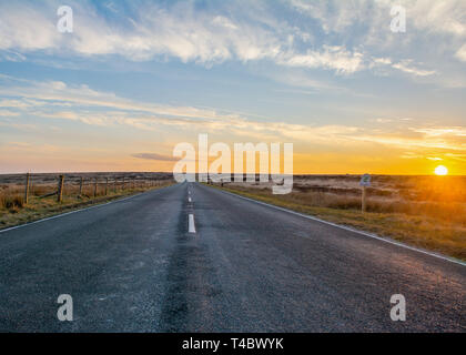 Marsden Moors, Yorkshire, UK, 13. April 2019. Einen goldenen Sonnenuntergang sinkt unter dem Horizont am Ende der Straße, die sich ihren Weg durch die Wildnis. Stockfoto