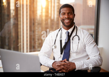 Portrait von lächelnden männlicher Arzt mit Stethoskop im Krankenhaus Büro Stockfoto
