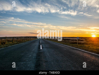 Marsden Moors, Yorkshire, UK, 13. April 2019. Einen goldenen Sonnenuntergang sinkt unter dem Horizont am Ende der Straße, die sich ihren Weg durch die Wildnis. Stockfoto