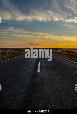 Marsden Moors, Yorkshire, UK, 13. April 2019. Einen goldenen Sonnenuntergang sinkt unter dem Horizont am Ende der Straße, die sich ihren Weg durch die Wildnis. Stockfoto