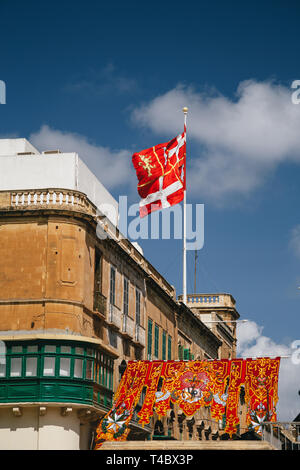 Die maltesische Flagge gegen einen blauen Himmel bei der festlich geschmückten Straße in der Altstadt von Valletta, die Hauptstadt von Malta. Beliebte touristische Destination und Stockfoto