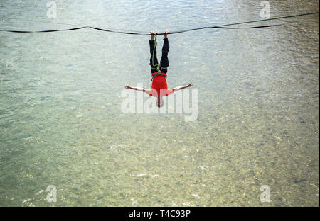 16 April 2019, Bayern, München: Die slackliner Lukas Irmler hängt auf der Slackline über der Isar. Foto: Sina Schuldt/dpa Stockfoto