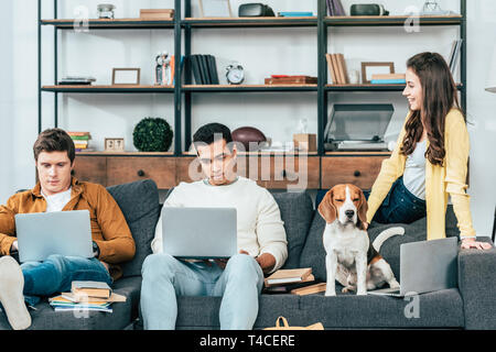 Drei fröhlichen multikulturellen Studenten auf Sofa und mit Laptops zu Hause sitzen Stockfoto