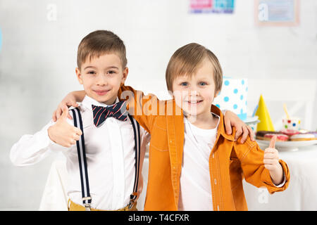 Adorable jugendliche Jungen Blick auf Kamera, umarmen und mit Daumen hoch während der Geburtstagsfeier Stockfoto