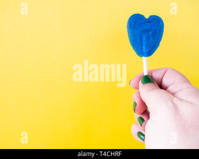 Eine Frau mit grün lackierten Nägel mit einem blauen Lutscher in der Hand und gelbem Hintergrund Stockfoto