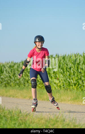 Jugendlich rollerblading im Sommer auf einer kleinen Straße, mit Helm und Protektoren Stockfoto