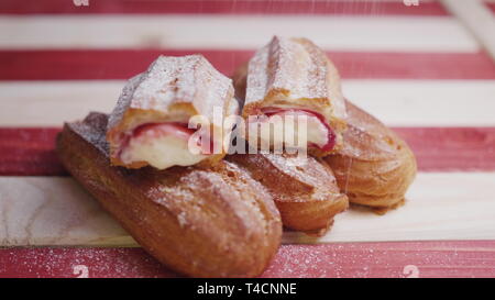 Slo motion Medium shot Video von frischem gesichert eclairs Cookies liegen auf einem rot-weiß gestreiften Holz- Fach und zur Besprengung mit Zucker Pulver. Ansicht von vorn Stockfoto