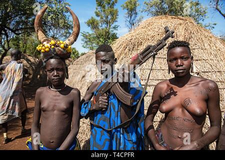 Junge Mädchen mit schmucknarben und der Mann mit der kalaschnikow vor der Hütte, Stamm der Mursi, Mago National Park, südlichen Nationen und Nationalitäten Stockfoto