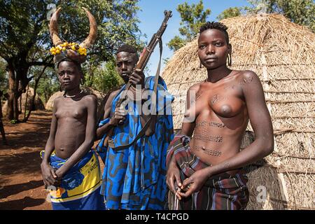 Junge Mädchen mit schmucknarben und der Mann mit der kalaschnikow vor der Hütte, Stamm der Mursi, Mago National Park, südlichen Nationen und Nationalitäten Stockfoto