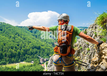 Touristische Kletterer zeigt seine Hand in der Entfernung auf einen Klettersteig Route in Baia De Fier, Gorj County, Rumänien. Männliche Kletterer mit Helm ausgerüstet, Klettern Stockfoto