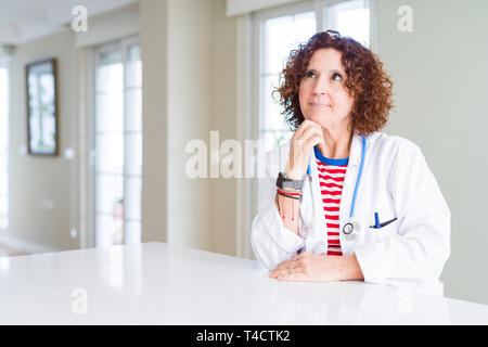 Leitender Arzt Frau mit medizinischen Robe an der Klinik mit der Hand am Kinn über die Frage denken, nachdenklichen Ausdruck. Lächelnd mit nachdenklichen Gesicht. Tun Stockfoto