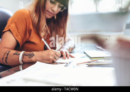 7/8 Schuß einer Künstlerin, eine Skizze auf einem Blatt Papier. Seitenansicht einer Illustrator einen kreativen Kunst an Ihrem Schreibtisch im Büro zu sitzen. Stockfoto