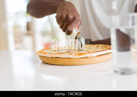 Nahaufnahme der afrikanischen Mann schneidet ein Stück Käse Pizza mit einem Cutter Stockfoto
