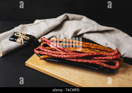 Polnische herkömmlichen Thin Würstchen kabanos auf schwarzem Hintergrund auf einer Platte von der Flasche. Kopieren Sie Platz. Fett essen Konzept. Stockfoto