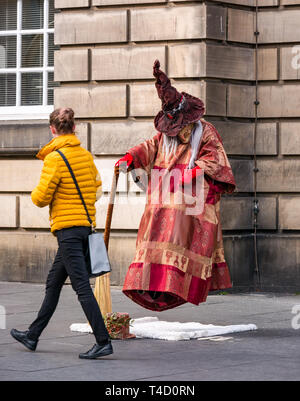 Frau vorbei gehen. Hexe und Besen levitation Street Performer lebende Statue handeln, Royal Mile, Edinburgh, Schottland, Großbritannien Stockfoto