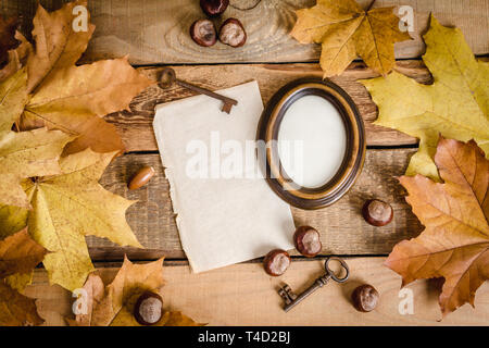 alten Rahmen, weißes Papier, Herbstlaub und Kastanien auf einem Holztisch Stockfoto