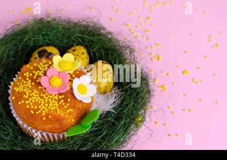 Muffins mit Streuseln, Blumen von Dichtmasse und Gelb Ostern Wachteleier in der grünen Nest in Pastell rosa Hintergrund. Ansicht von oben. Kopieren Sie Platz. Ea Stockfoto