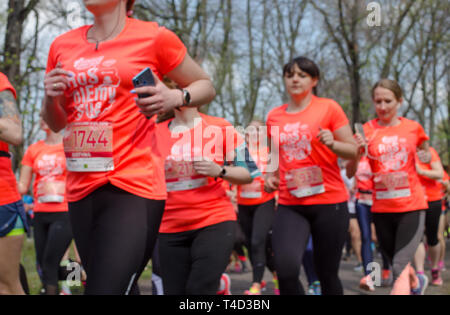 Riesige Gruppe von Frauen in orangefarbenen T-Shirts mit Zahlen laufen Marathon im Park im Frühling. Wroclaw, Polen - 7 April, 2019. Stockfoto