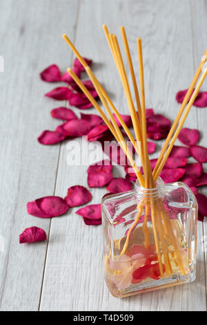 Reed Diffuser mit Duft im Glas mit Rosenblättern auf einem grauen Holz Hintergrund Stockfoto