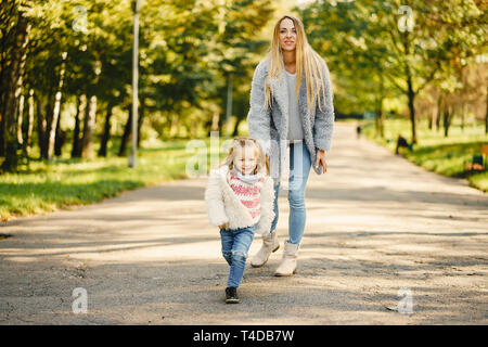 Junge blonde Mutter hinter ihr super energetische toddler Tochter in einem sonnigen Park Stockfoto