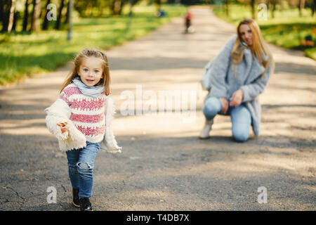 Junge blonde Mutter hinter ihr super energetische toddler Tochter in einem sonnigen Park Stockfoto