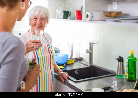 Ältere Frau/die Großmutter Kochen in eine moderne Küche mit ihrer Enkelin, Weinprobe, einer grünen Smoothie (flacher DOF; Farbe getonte Bild) Stockfoto