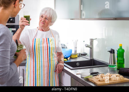 Ältere Frau/die Großmutter Kochen in eine moderne Küche mit ihrer Enkelin, Weinprobe, einer grünen Smoothie (flacher DOF; Farbe getonte Bild) Stockfoto