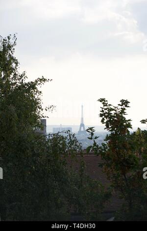 Grüne Blätter auf den Bäumen im Vordergrund. Paris, Frankreich Skyline im Dunst (Nebel), inklusive Eiffelturm, zwischen den Bäumen eingerahmt. Stockfoto