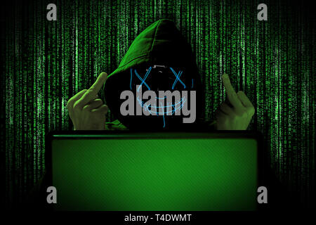 Hacker mit mittleren Finger Geste Provokation blau leuchtende Maske hinter Notebook Laptop vor grüne Quelle binärer Code Hintergrund Internet cyber Stockfoto