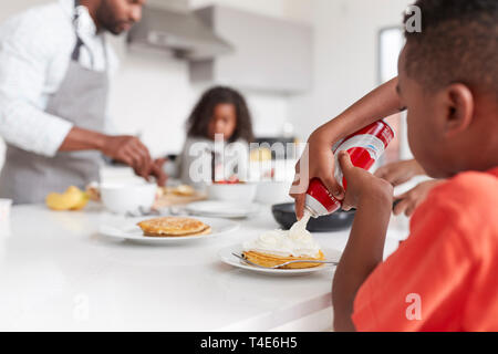 Junge hinzufügen Creme zu Pfannkuchen als Familie genießen Sie Ihr Frühstück in der Küche zu Hause zusammen Stockfoto