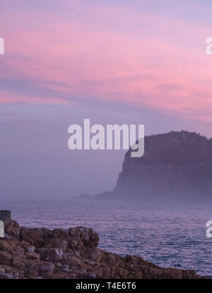 Die Staats- und Regierungschefs, Knsyna, Garden Route, Südafrika. Felsvorsprung an der Spitze der Lagune, in Nebel bei Sonnenuntergang fotografiert. Stockfoto