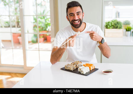 Schöner Mann lächelt glücklich Genießen Essen frische Bunte asiatische Sushi mit Stäbchen Stockfoto