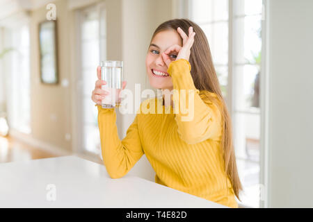 Schöne junge Mädchen Junge trinkt ein frisches Glas Wasser mit glücklichen Gesicht lächelnd tun ok Zeichen mit der Hand auf Auge schauen durch die Finger Stockfoto